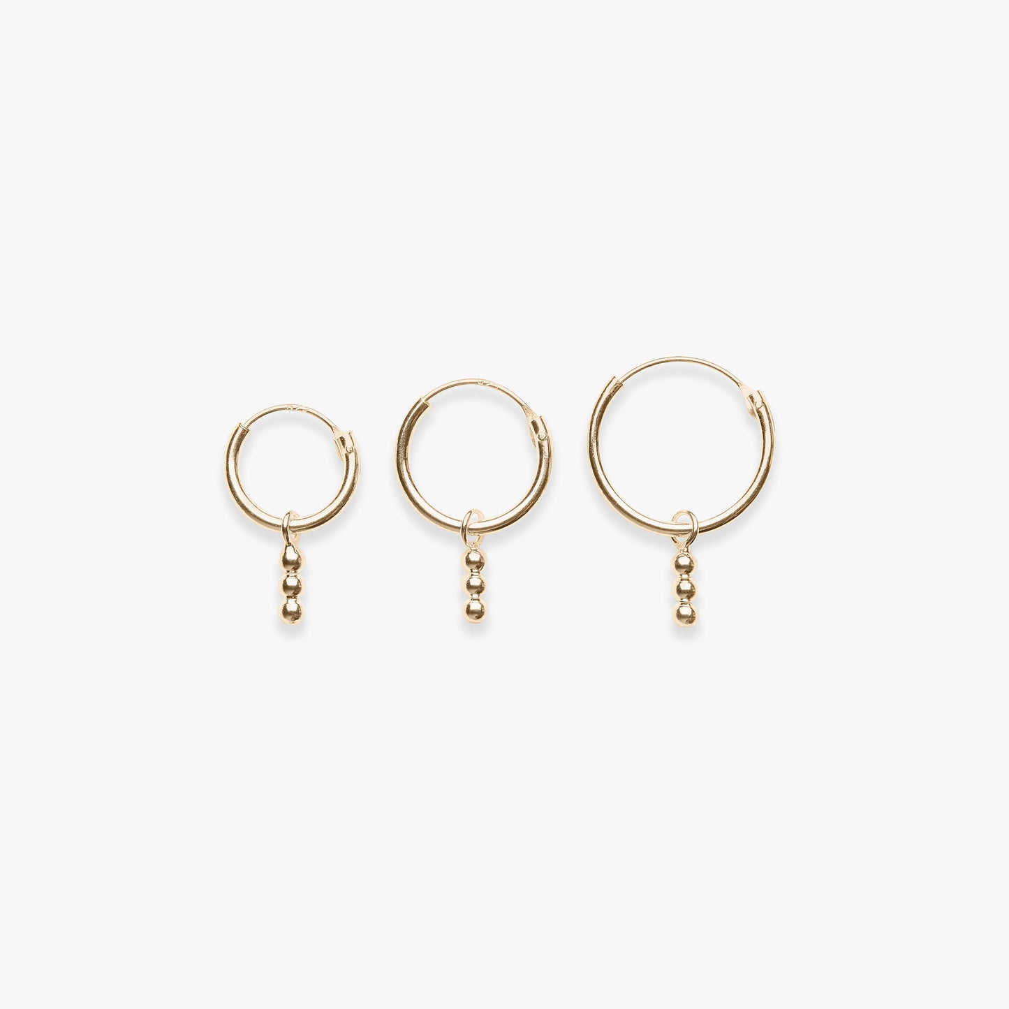 Three gold hoop earrings with small dangling beads on a white background