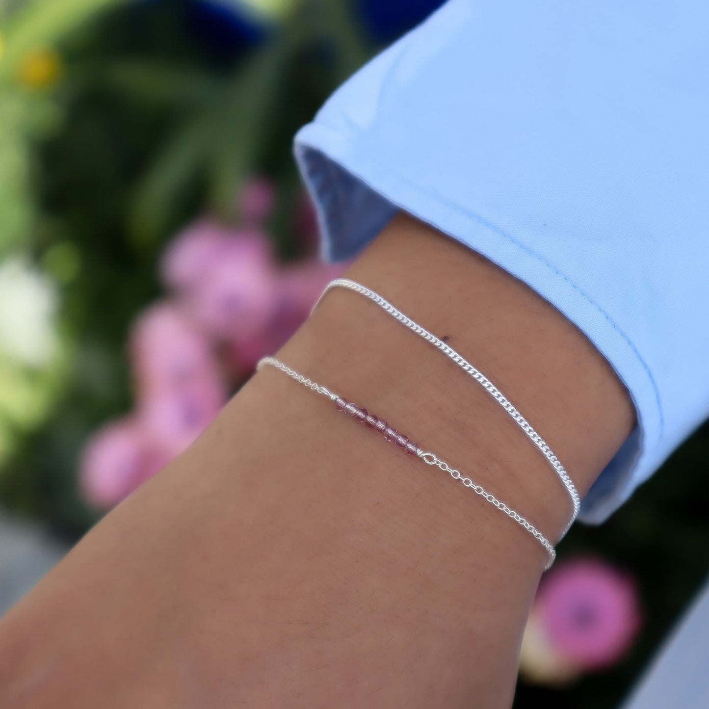 Silver anklets on a person's wrist with a blurred floral background