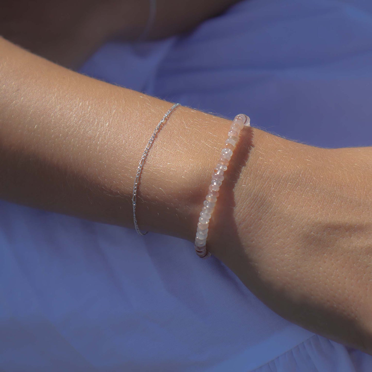 Close-up of a wrist wearing two delicate bracelets against a blue fabric background