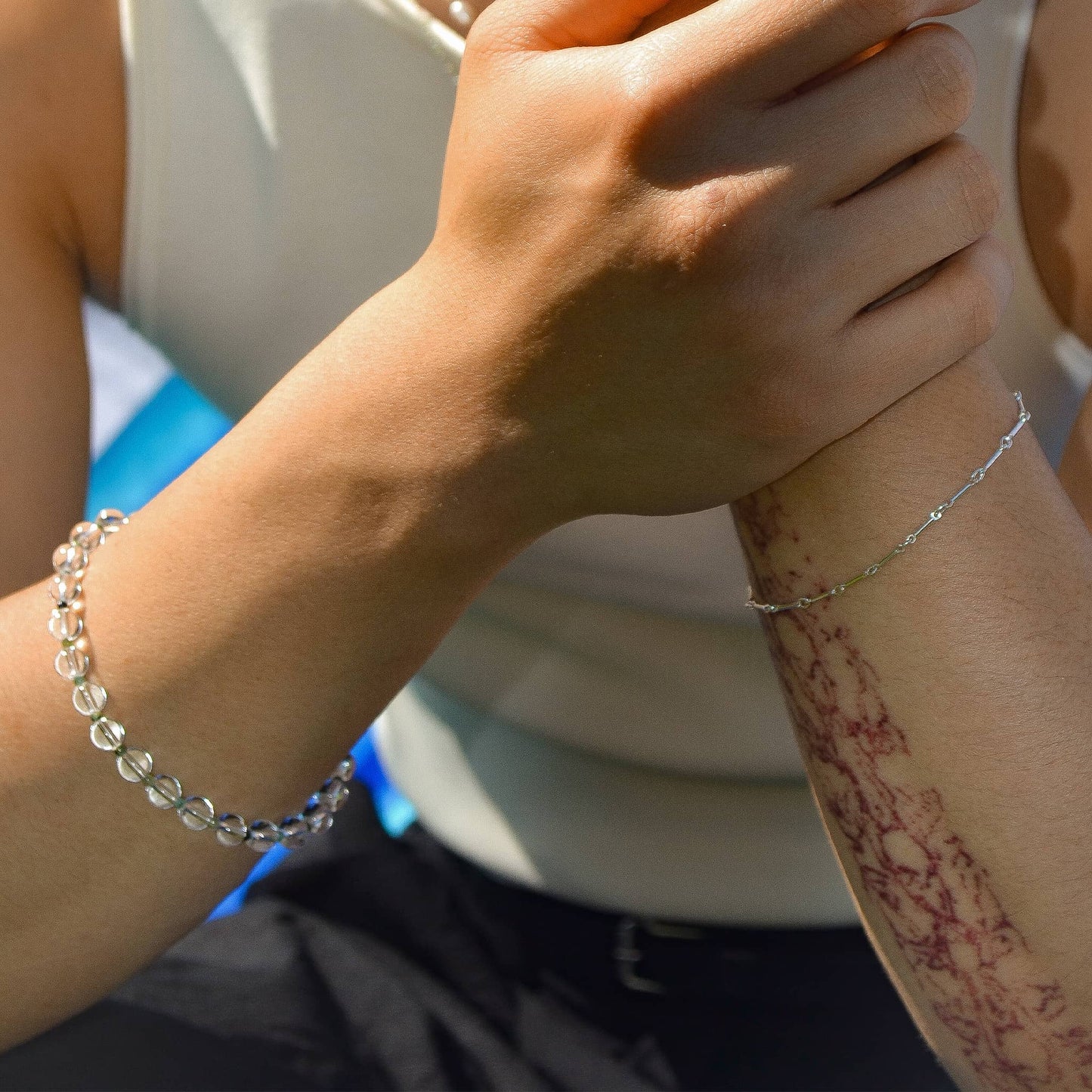 Two hands holding each other with bracelets on wrists, blurred background