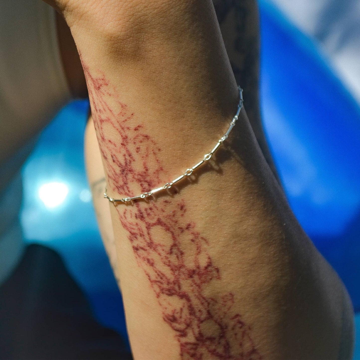 Close-up of a person's arm with red tattoo and a silver bracelet against a blurred background.