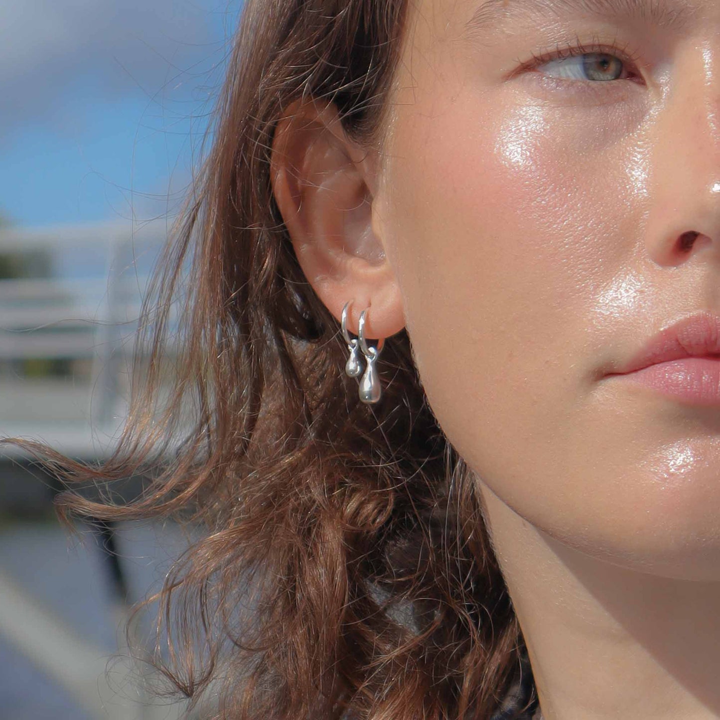 Close-up of a person wearing silver earrings with a blurred outdoor background