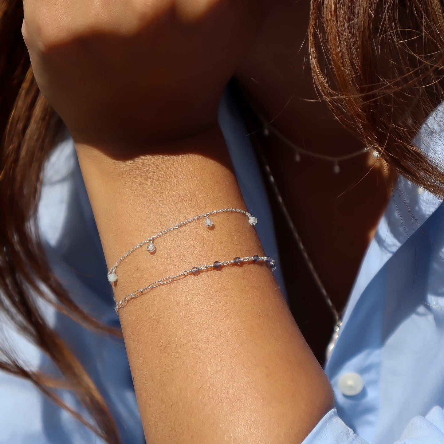 Close-up of a person's arm wearing multiple delicate bracelets with a blurred background.