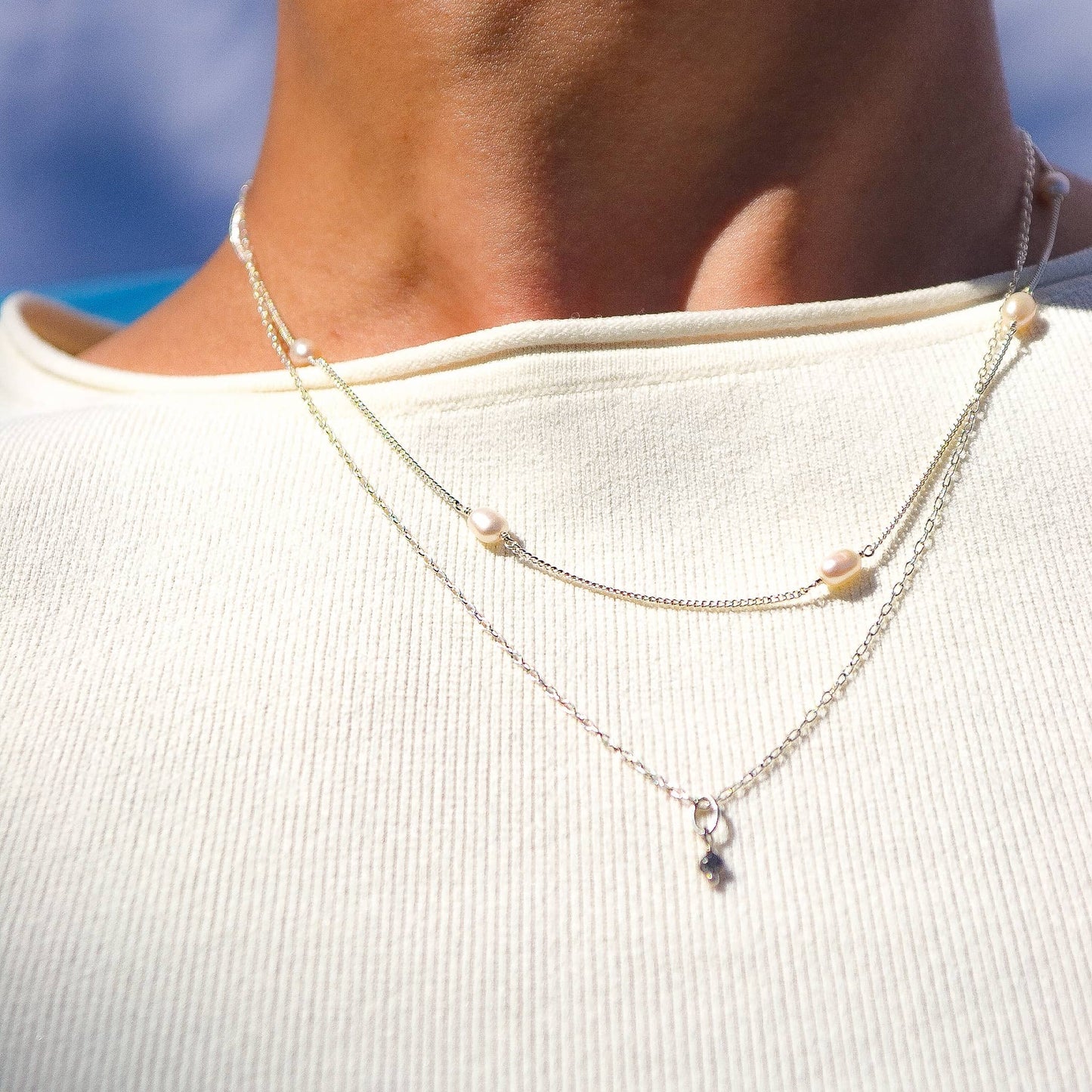 Close-up of a person wearing a layered necklace with a blurred background