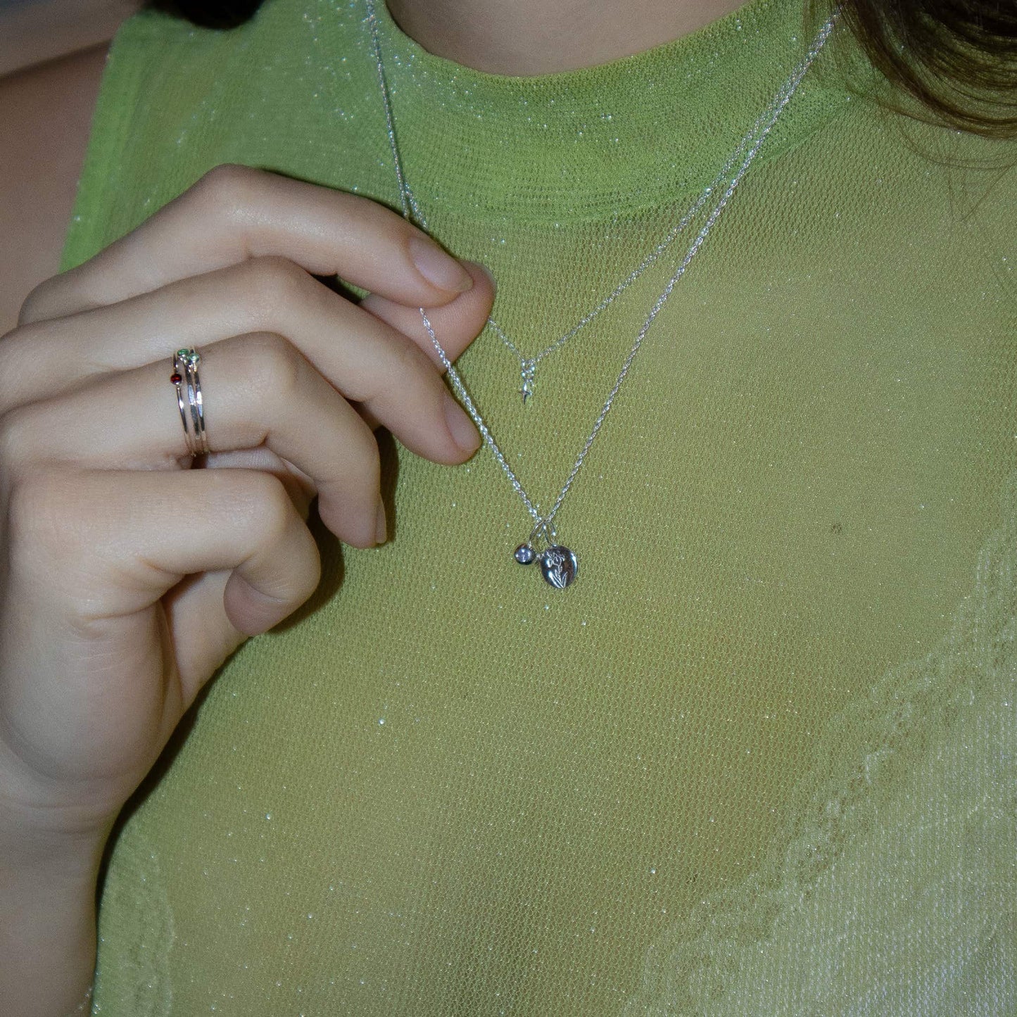 Person wearing a green top with a necklace and rings on a plain background