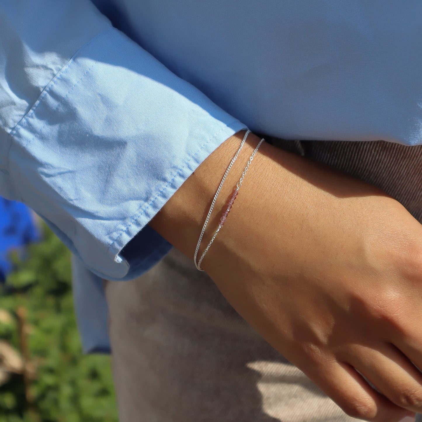 Close-up of a person wearing a silver bracelet with a blurred natural background