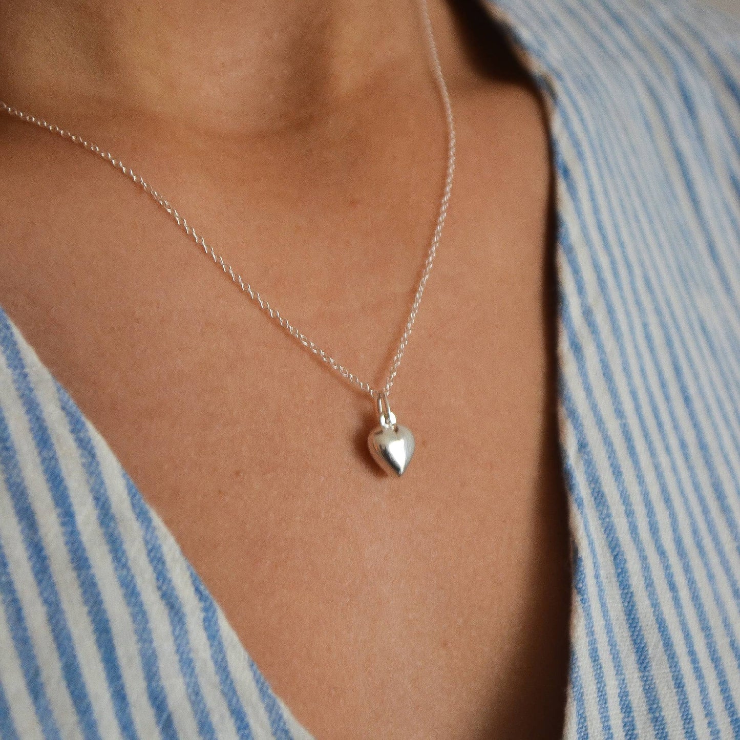 Silver heart-shaped pendant necklace on a person wearing a striped shirt