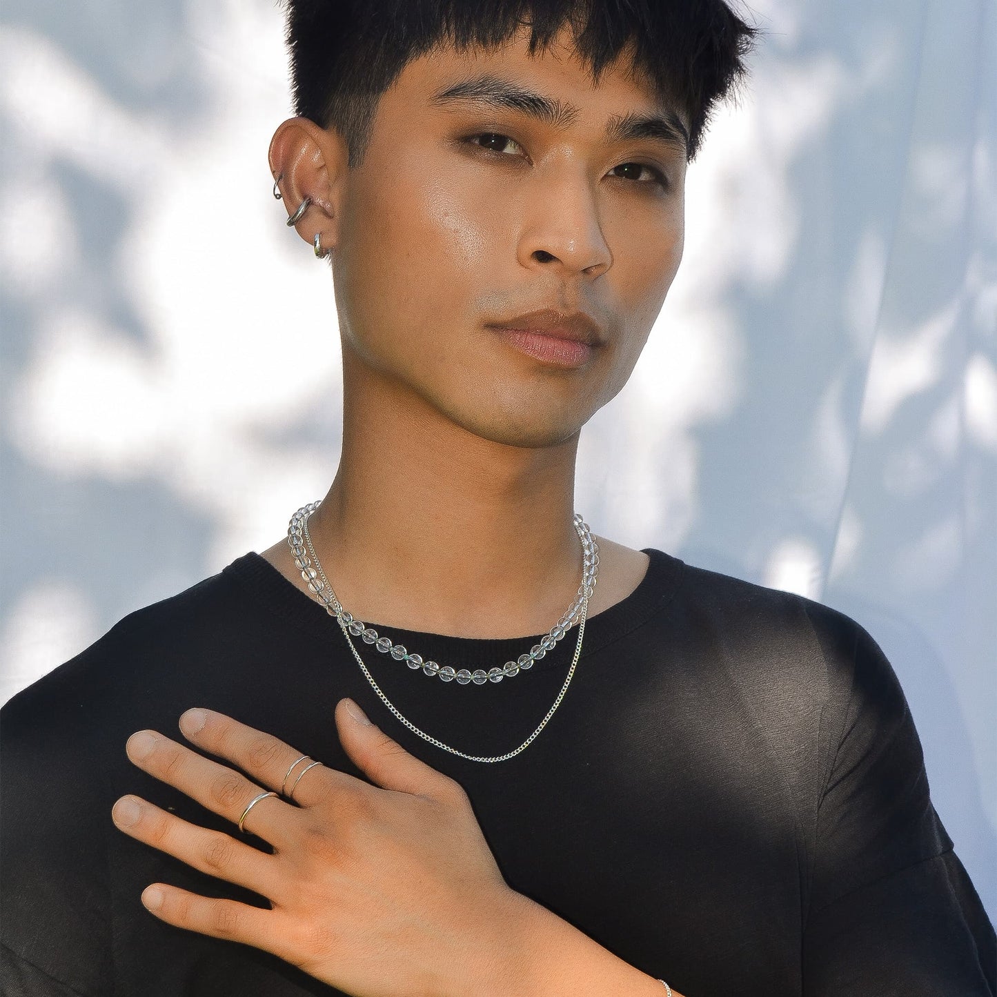Man wearing a black shirt and silver necklace with a blurred white background