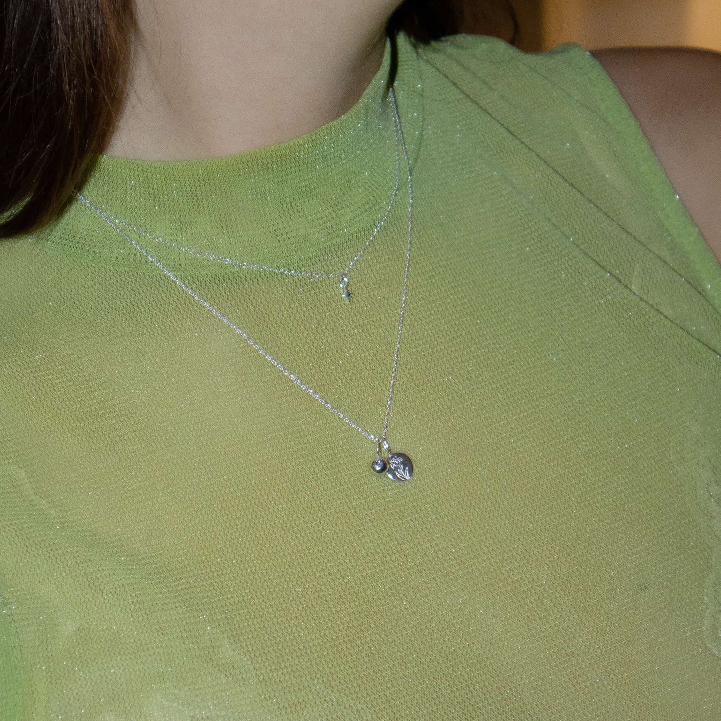 Necklace with a birthflower pendant worn by a person in a green top.