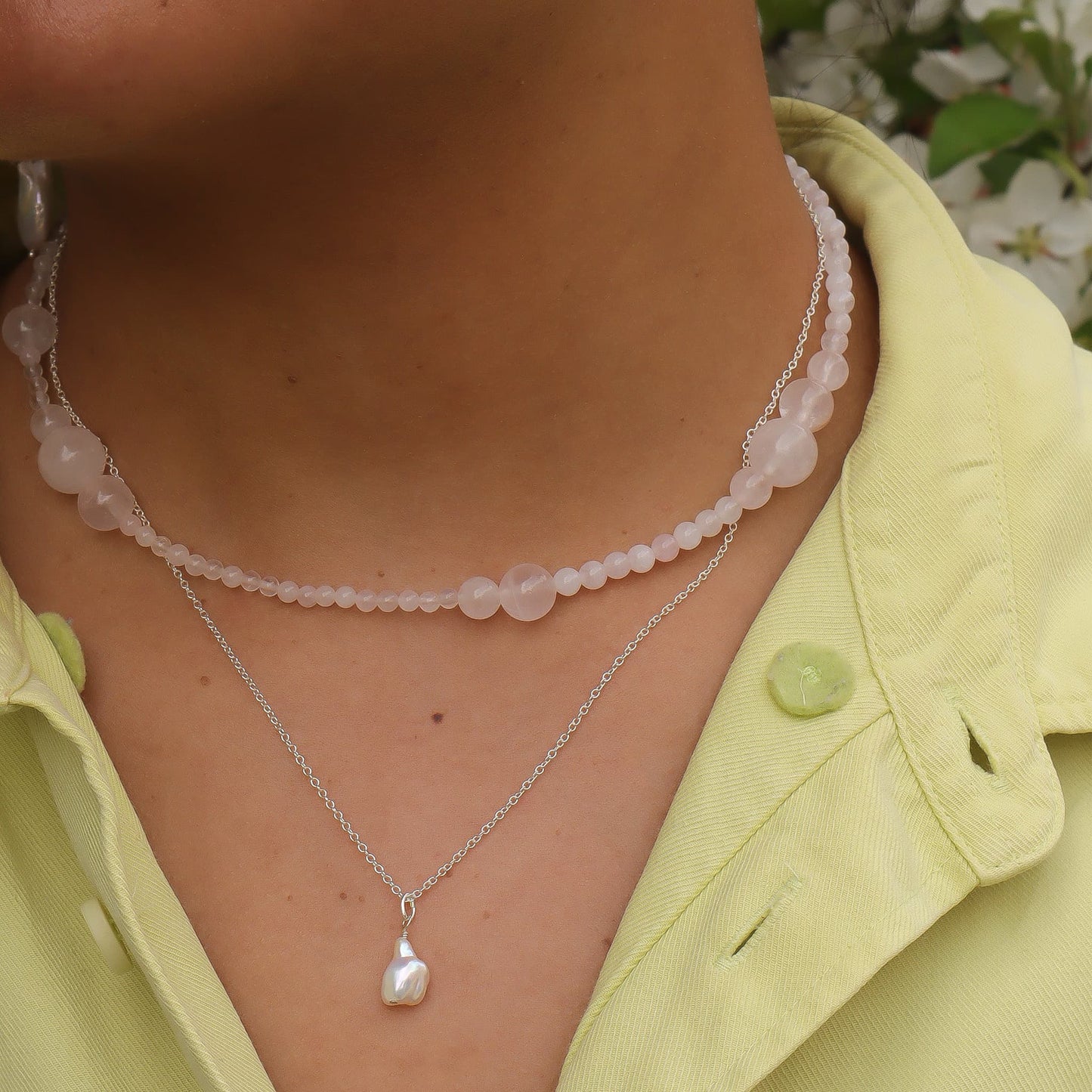 Close-up of a person wearing two necklaces with a light background