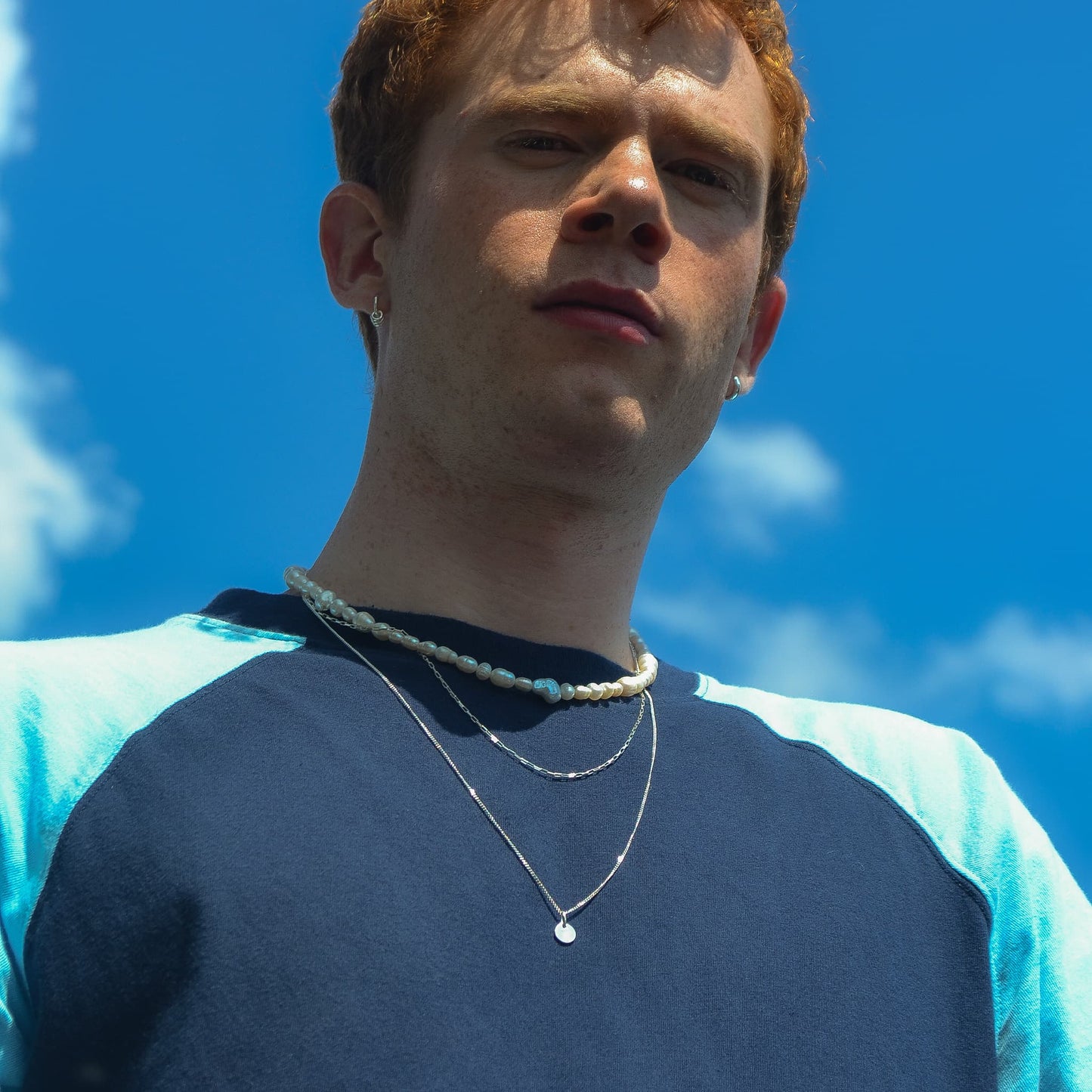 Person wearing layered necklaces against a blue sky