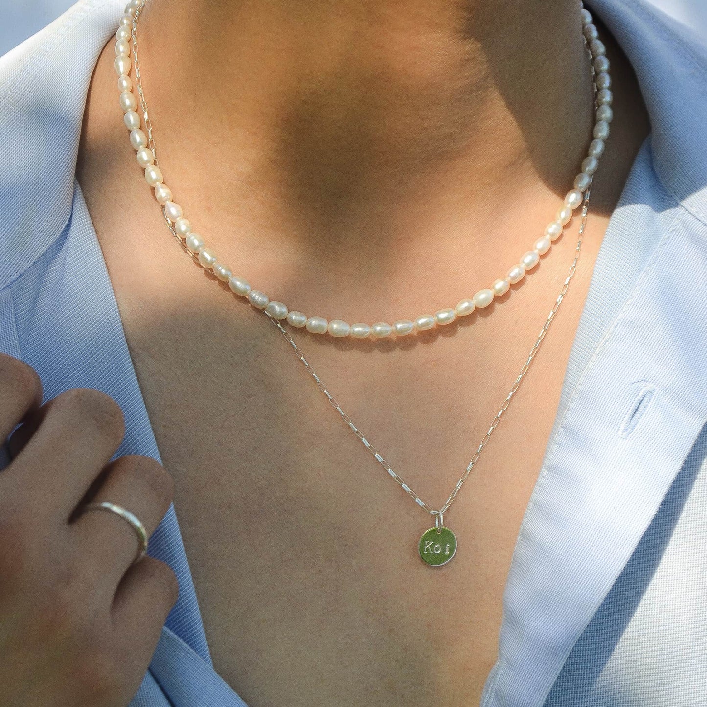 Person wearing a pearl necklace and a silver necklace with a green pendant.