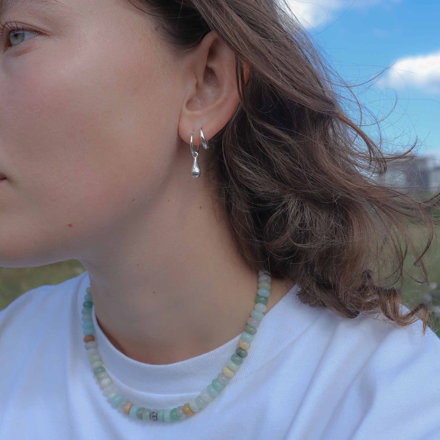 Close-up of a person wearing silver hoop earrings with a blurred natural background