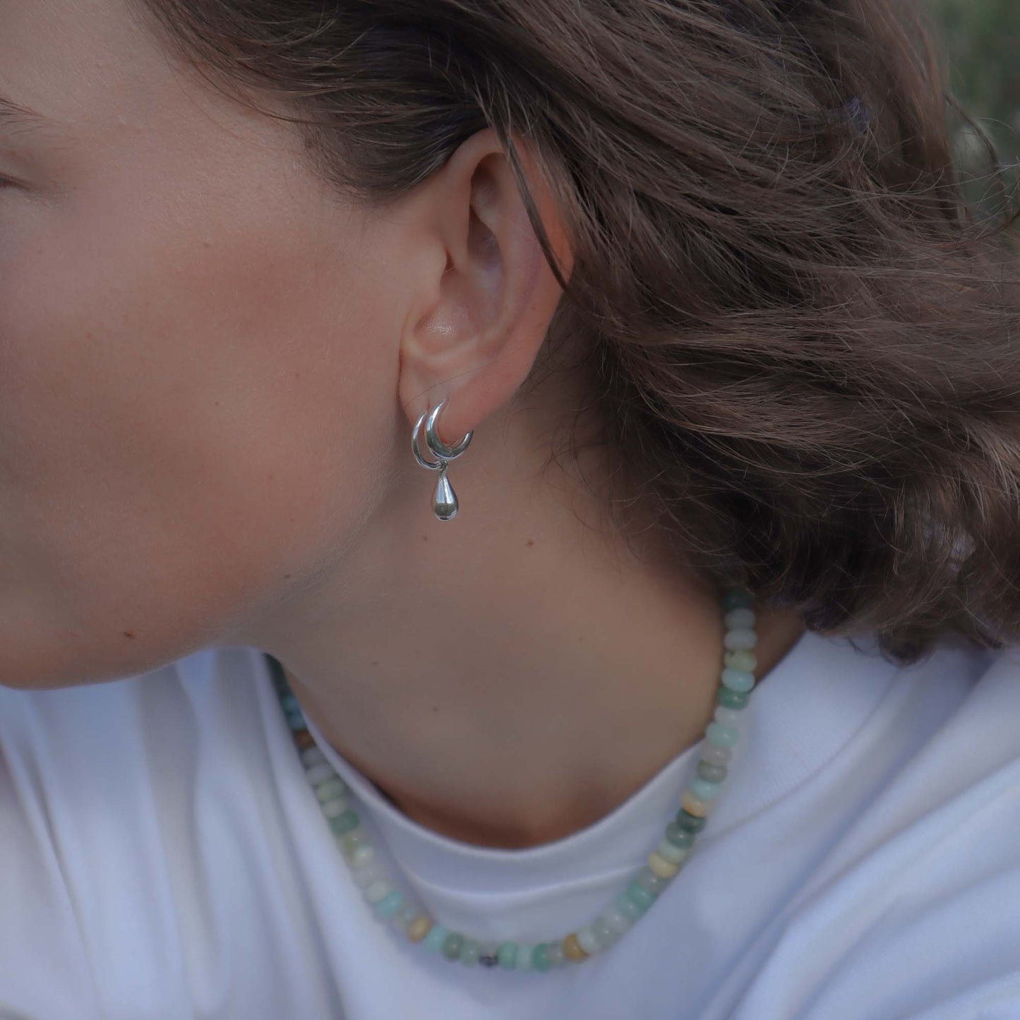 Close-up of a person wearing a silver earring and a beaded necklace.