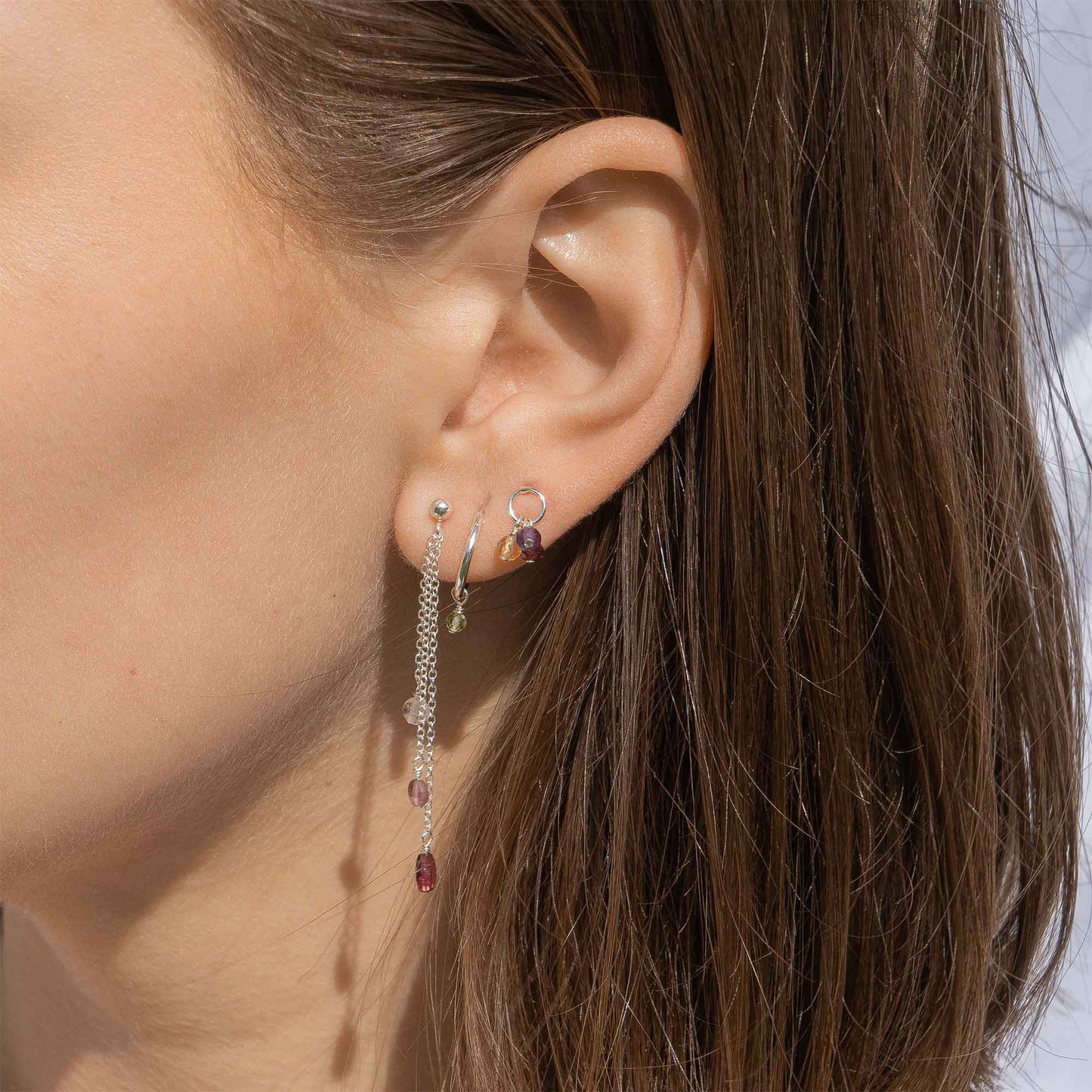Close-up of an ear wearing a silver earring with red gemstones and a small hoop earring.