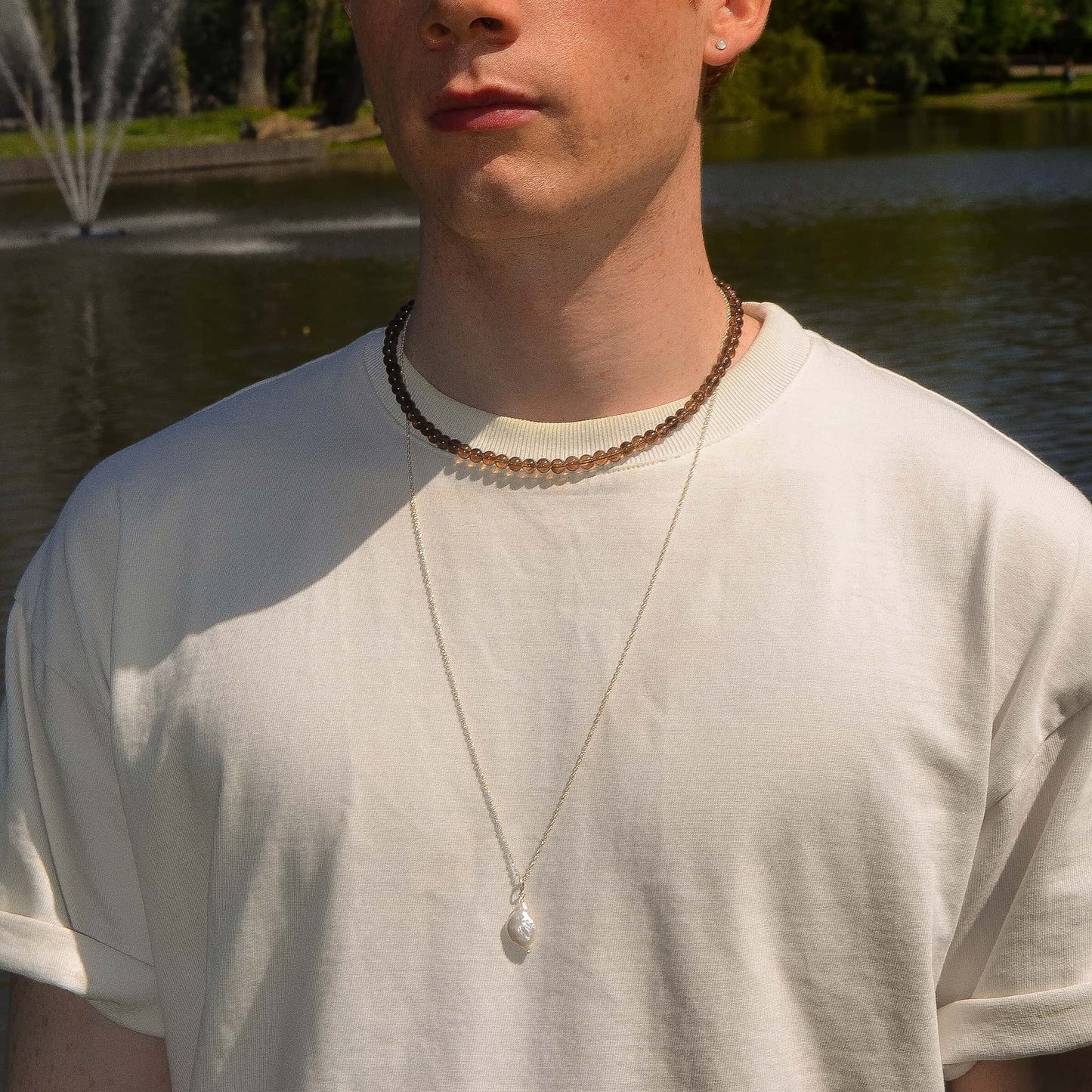 Person wearing a necklace with a pendant in front of a fountain and water.