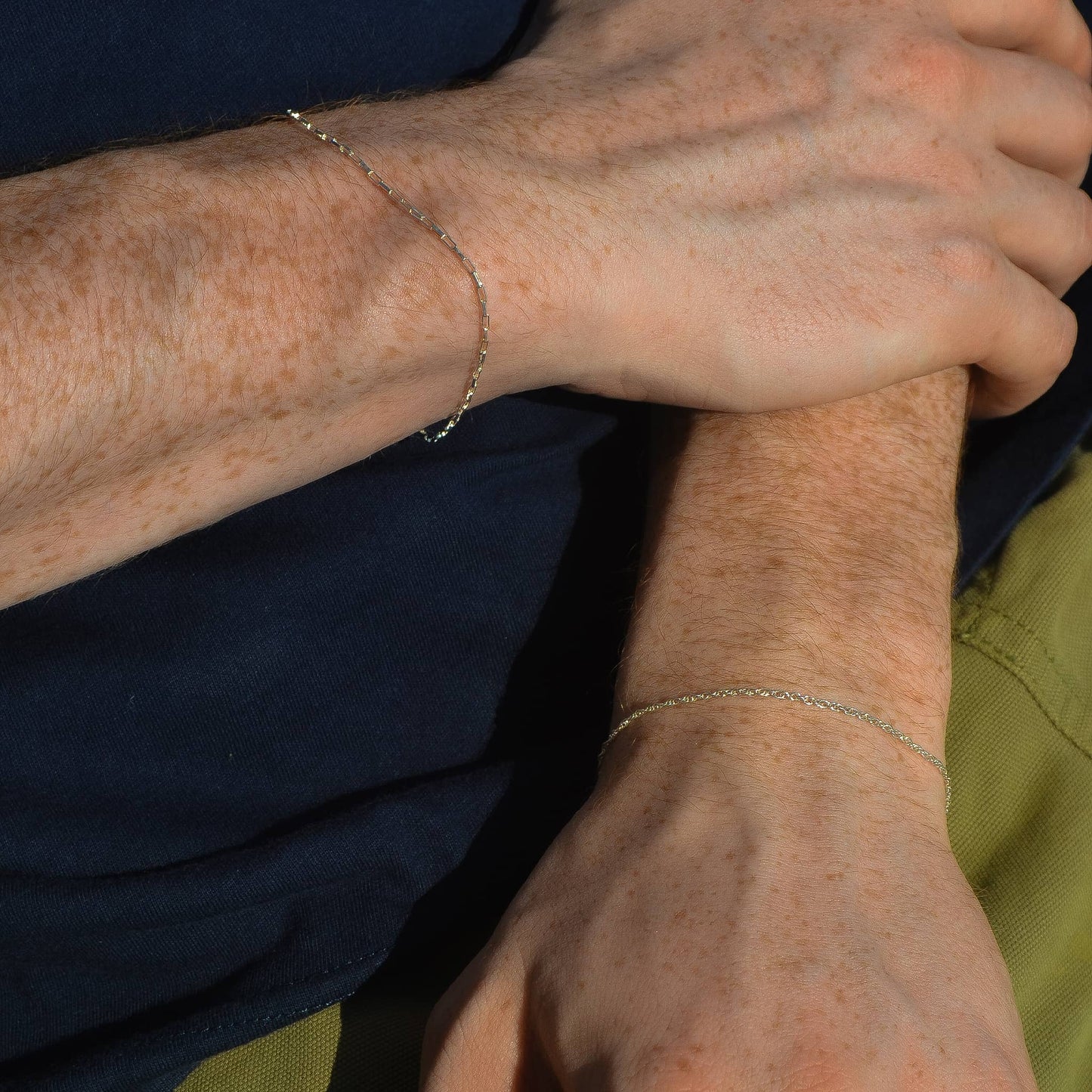Close-up of a person's arm with a bracelet, wearing a dark shirt and green pants.