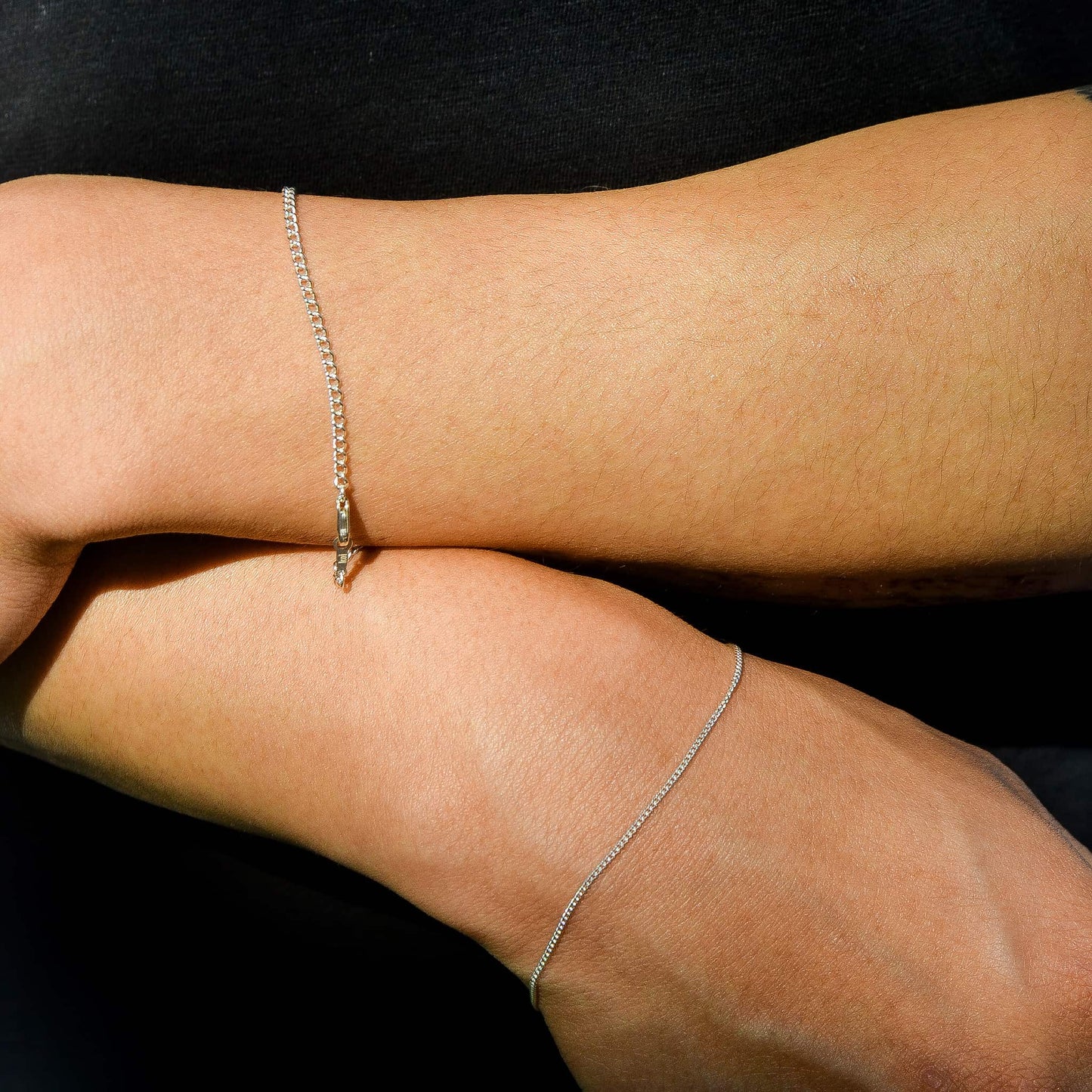 Silver bracelets on a person's wrists against a black background