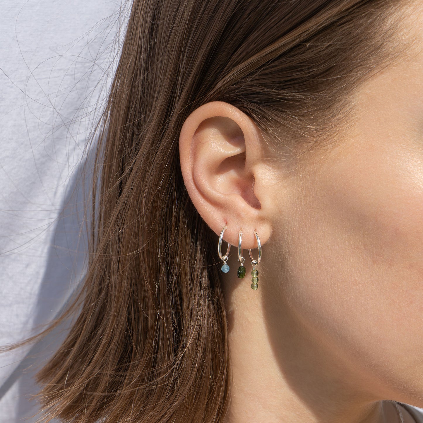 Close-up of an ear wearing multiple hoop earrings with a neutral background