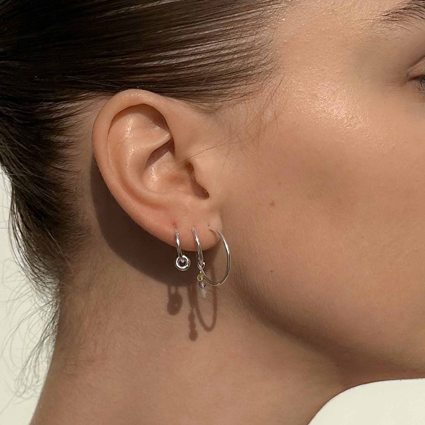 Close-up of a person wearing two silver hoop earrings with small charms.