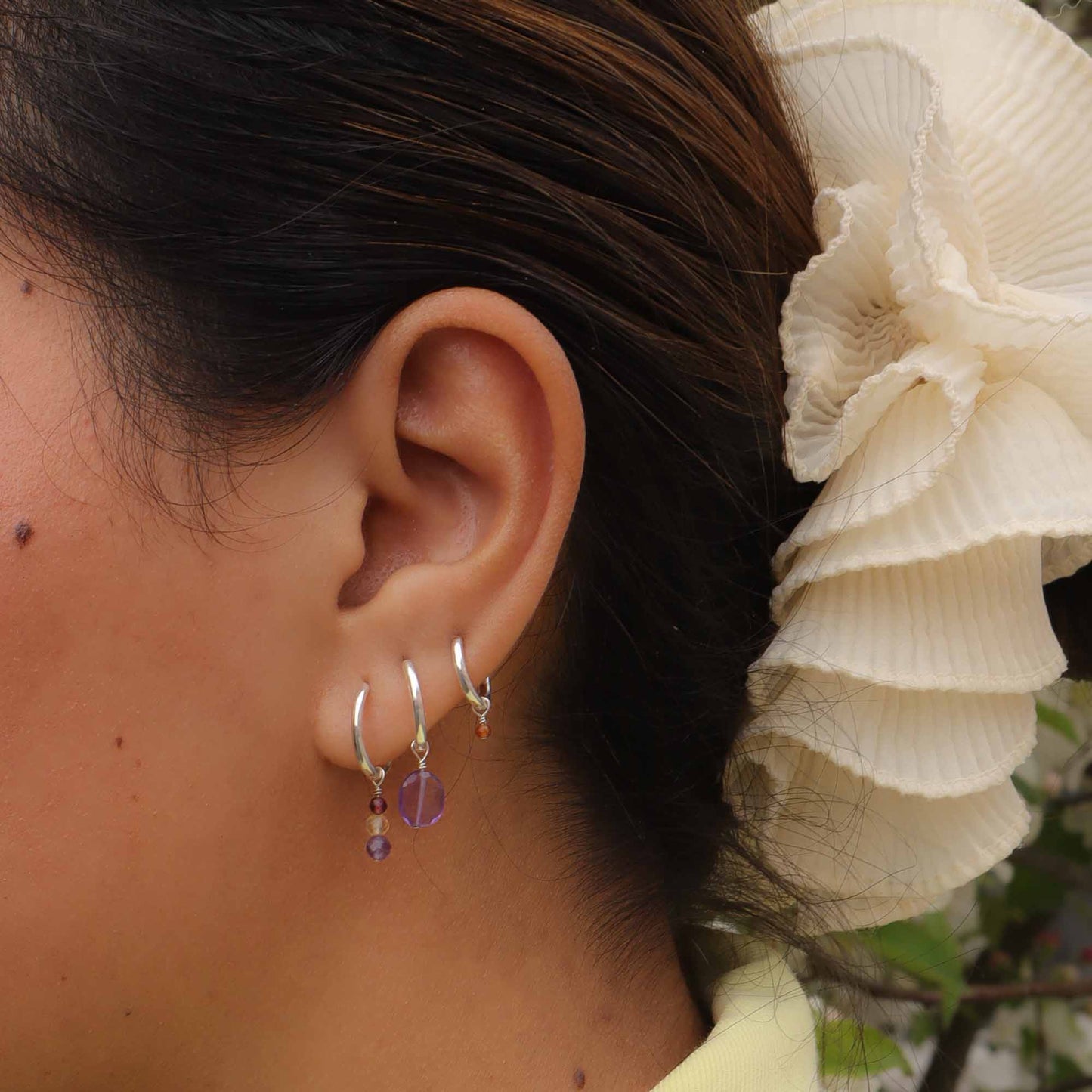 Close-up of an ear wearing silver hoop earrings with purple beads, blurred background