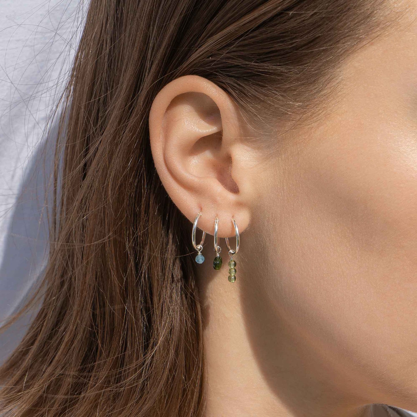 Close-up of an ear wearing three hoop earrings with gemstones against a neutral background