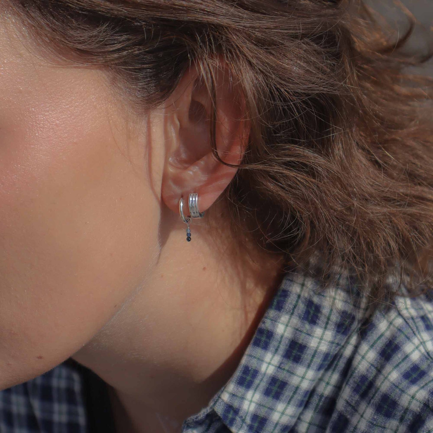 Close-up of an ear with a silver earring, wearing a plaid shirt.