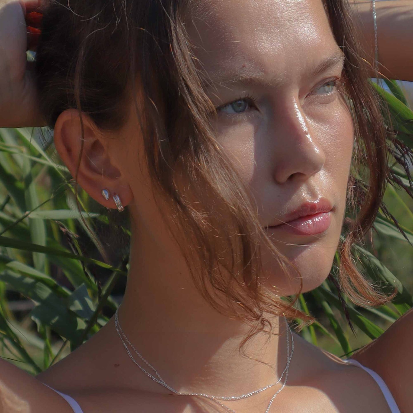 Woman with sun-kissed skin and light makeup, wearing a necklace, against a natural background.