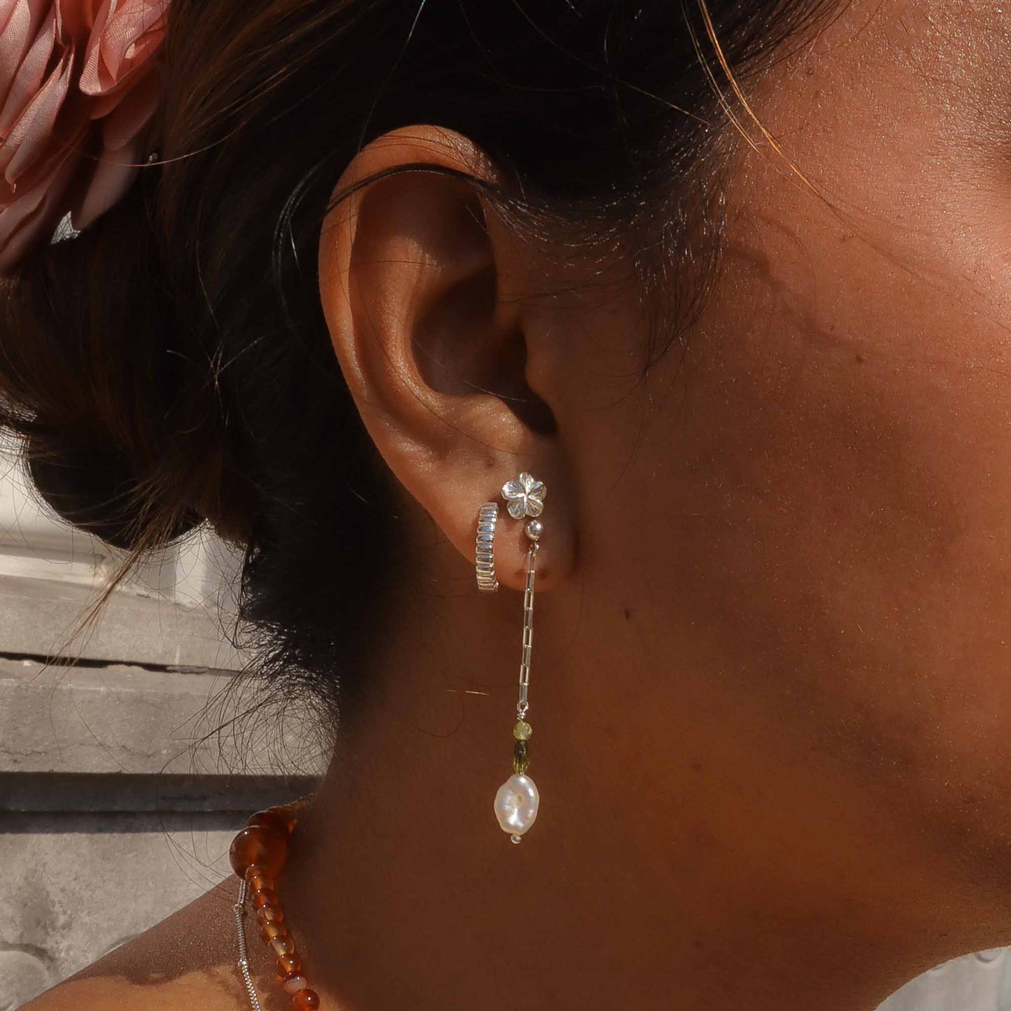 Close-up of an ear wearing a floral earring with a pearl drop, with a blurred background.