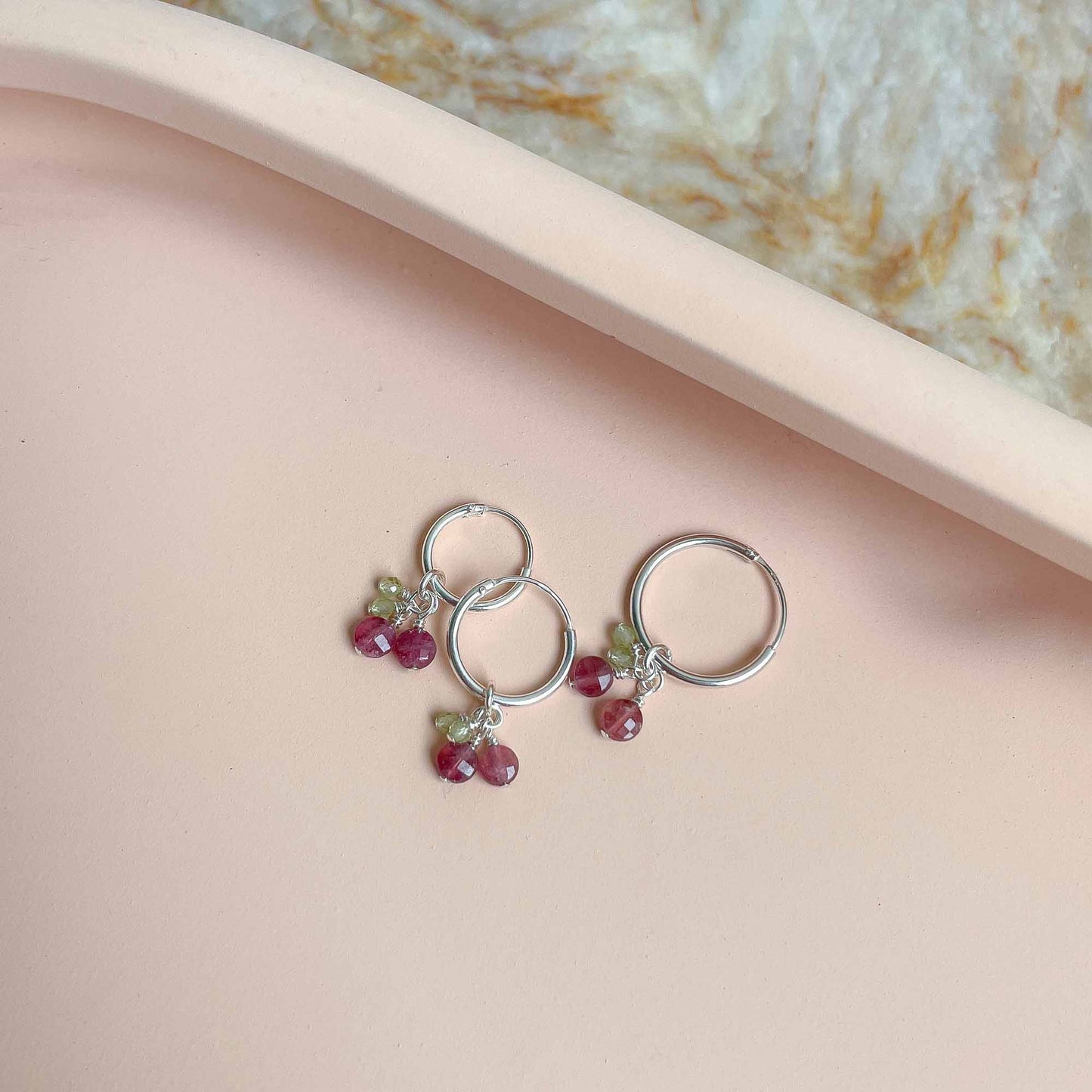 Silver earrings with gemstones on a pink surface