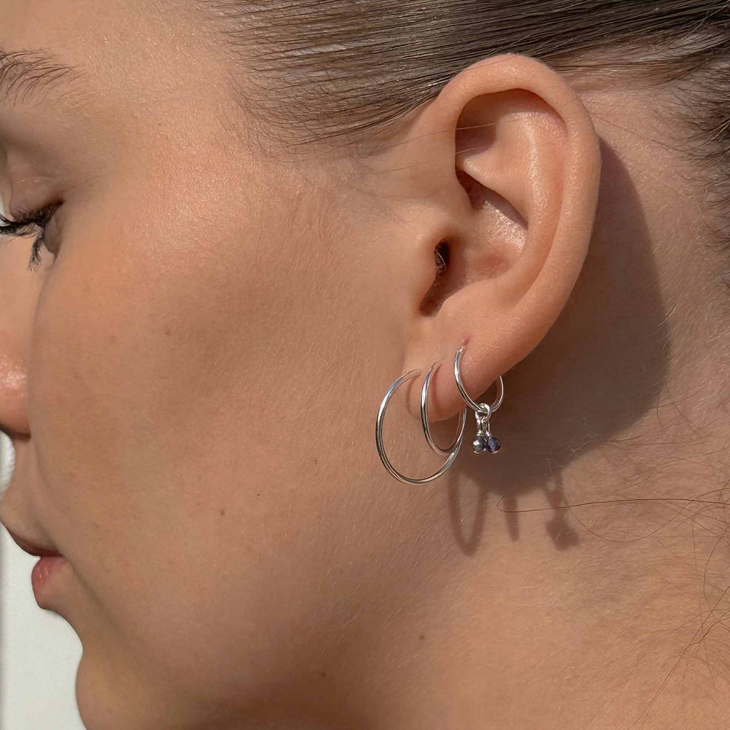 Close-up of a person wearing silver hoop earrings with a neutral background