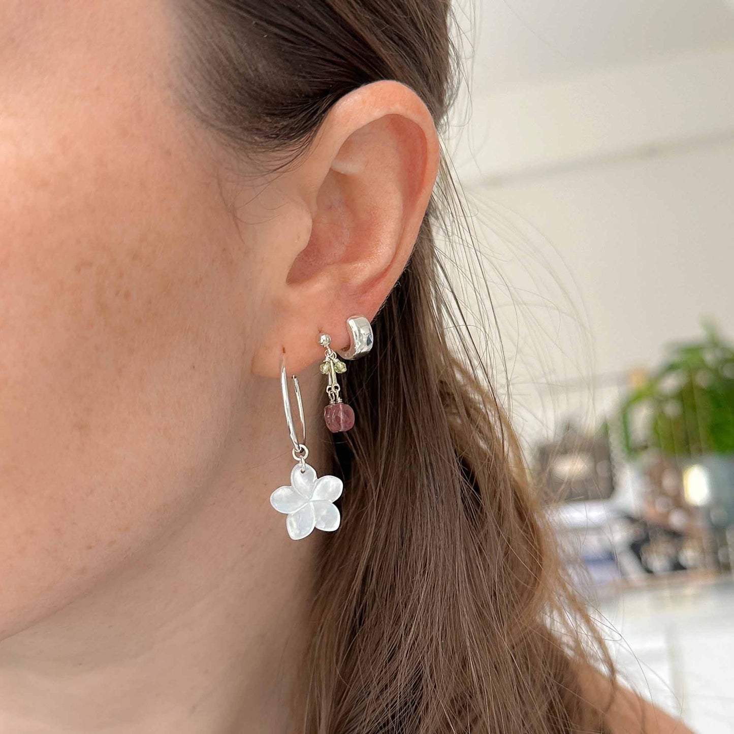 Close-up of a person wearing silver flower earrings with a blurred background