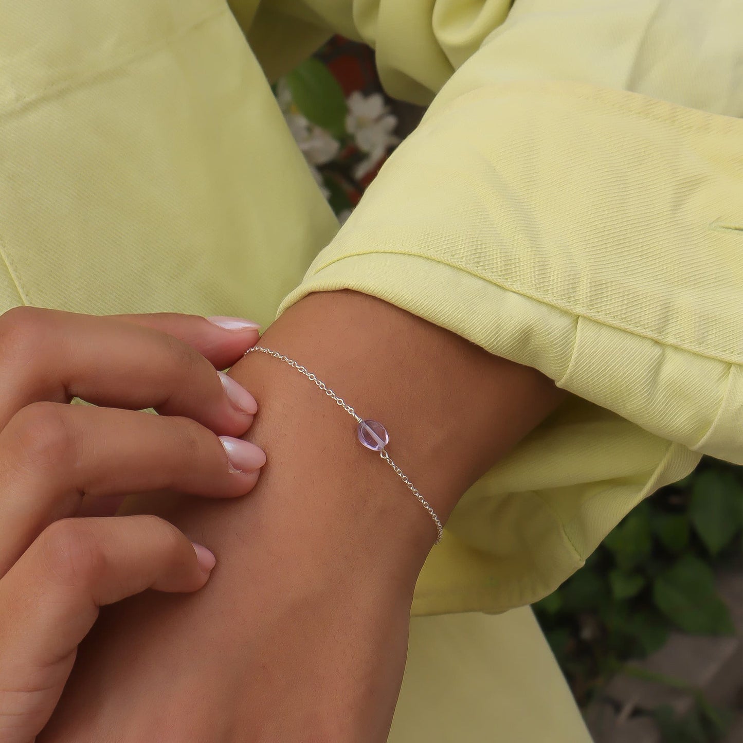 Person wearing a silver bracelet with a purple gemstone on a light green outfit.