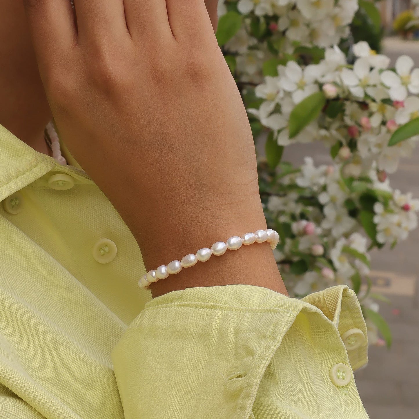 Person wearing a pearl bracelet with a blurred floral background