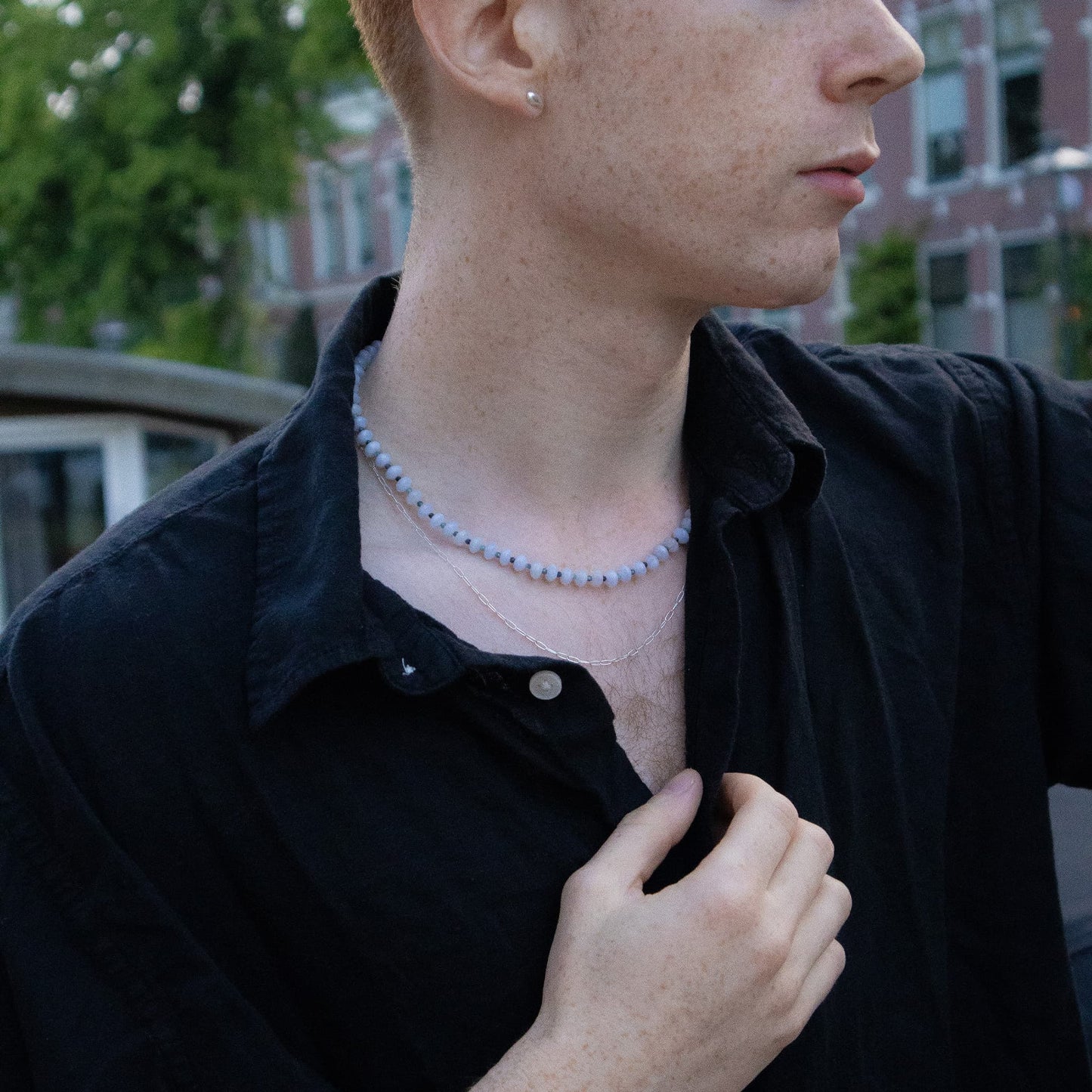 Person wearing a black shirt with a necklace, outdoors.